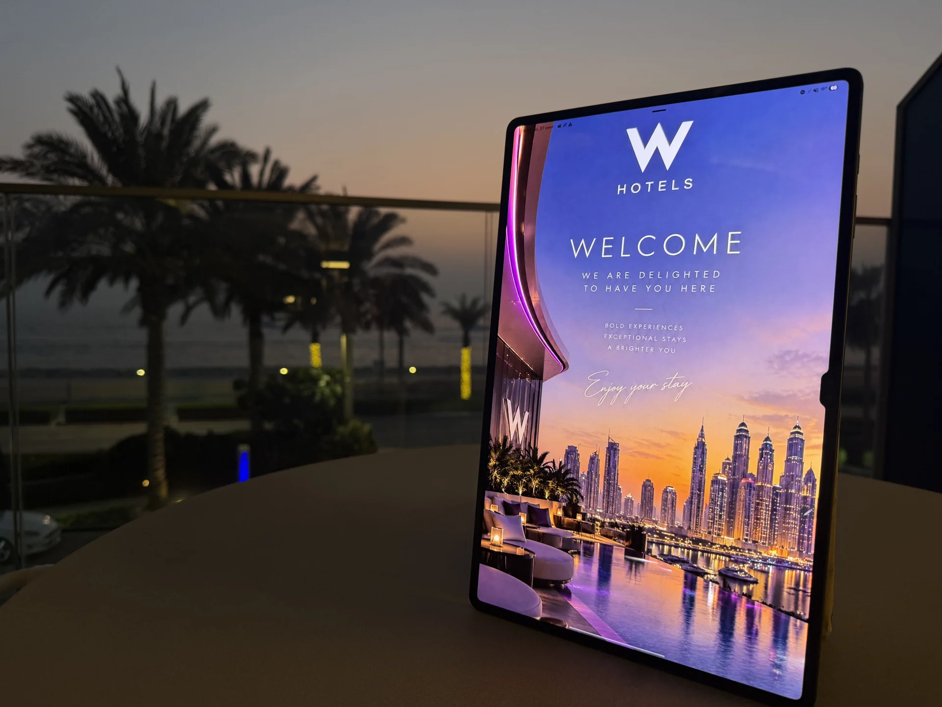 In-room tablet with a hotel welcome screen beside a sea-view window